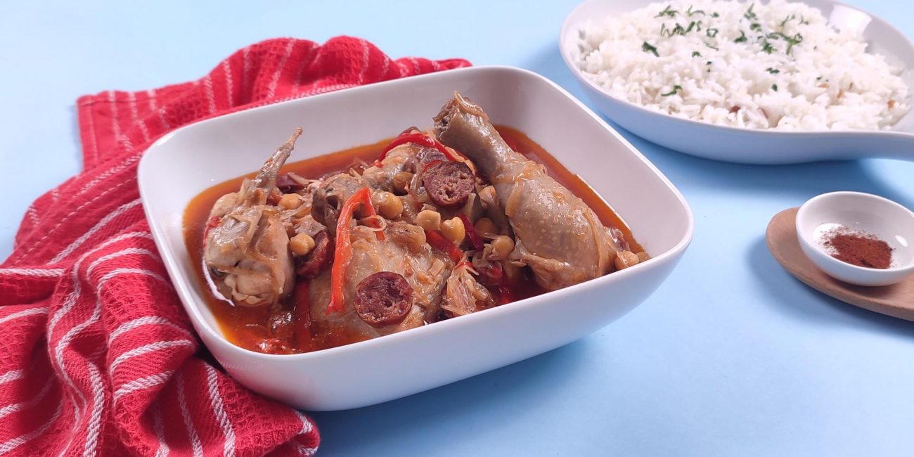 chicken callos in a rectangular bowl and rice in the background